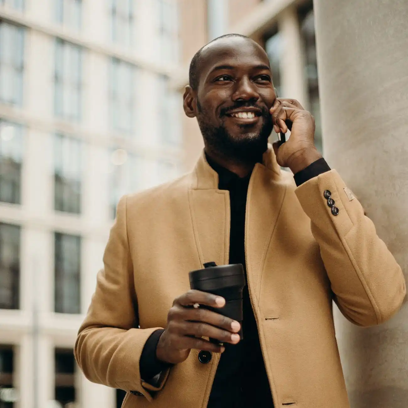 Well-dressed black male talking on smartphone with a reusable coffee mug in hand